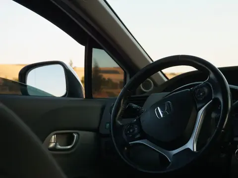 A car door open beside the steering wheel, its side glass and mirror in view